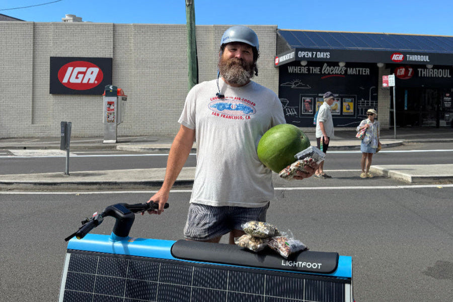 Man with a watermelon standing next to a solar-powered vehicle on a street.